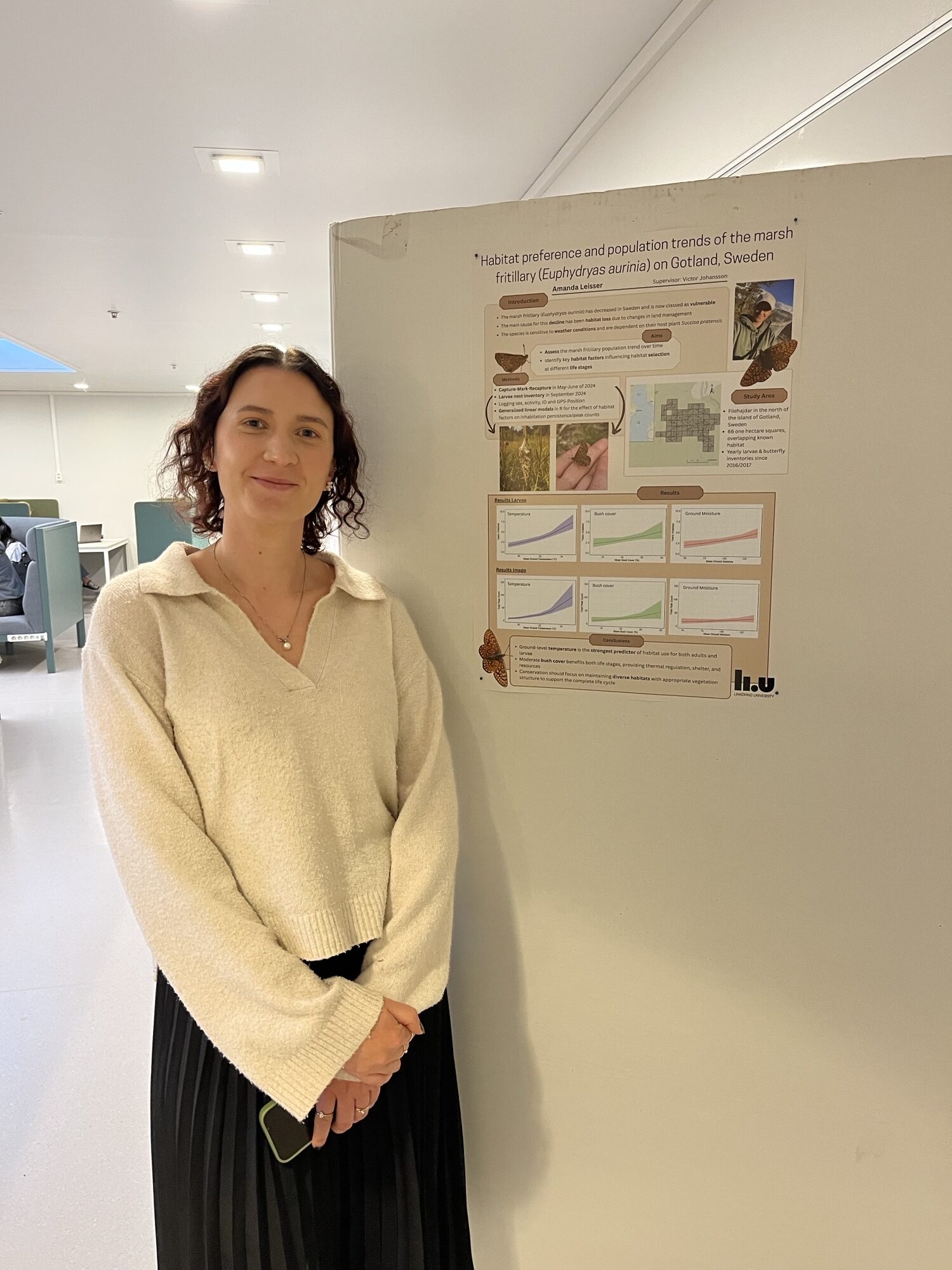 Woman in cream sweater standing beside a research poster about marsh habitat in Gotland, Sweden