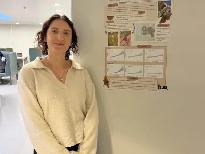Woman in cream sweater standing beside a research poster about marsh habitat in Gotland, Sweden