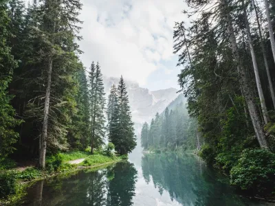A calm river flows between dense evergreen forests with misty mountains visible in the distance