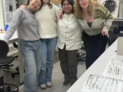 Four people smiling together in a laboratory with insect specimens and pinned insects on a table